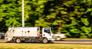 A white garbage truck running swiftly through the highway early in the morning.