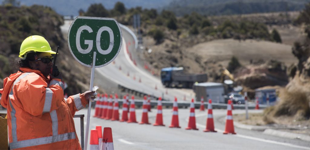 Construction worker holds up a "go" sign at roadworks